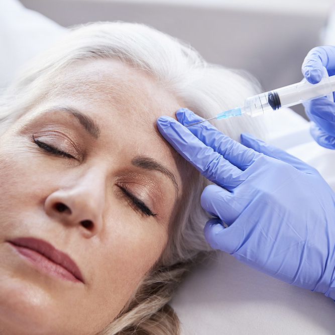 Beautician Giving Mature Female Patient Botox Injection In Forehead